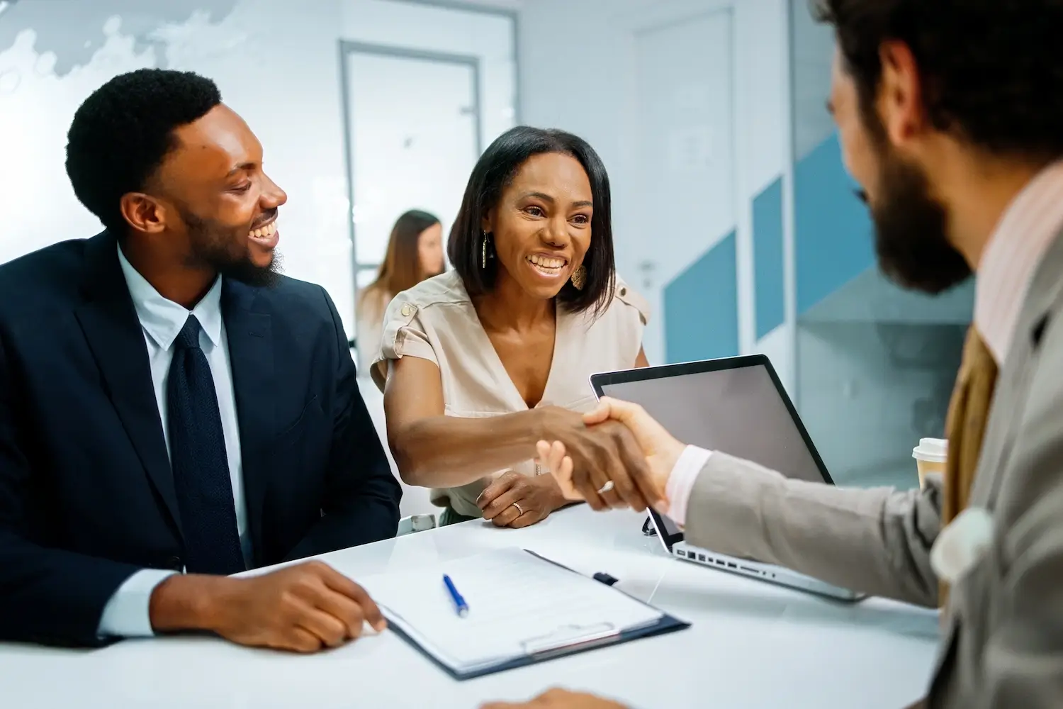 Safeline-About-Hero Diverse business professionals smiling and shaking hands in a bright, modern office with documents and a laptop on a conference table.